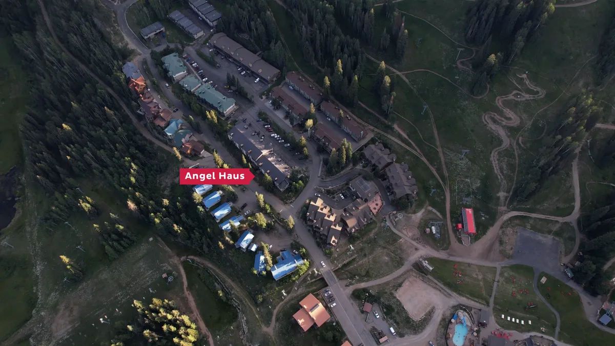 This exterior shot captures the Angel Haus buildings with distinctive blue roofs, the pool and hot tub area, winding mountain trails, and a cluster of neighboring lodges. The setting exudes relaxation and a sense of outdoor adventure, showing how close the amenities and outdoor activities are.