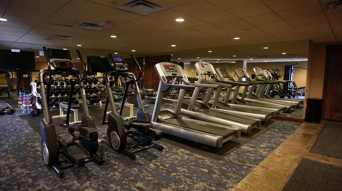 This image features a row of treadmills and elliptical machines, as well as a dumbbell rack, all arranged in a well-lit fitness area. The space is organized for guests to engage in cardio workouts or weight training, with ample room for multiple people to exercise at once.